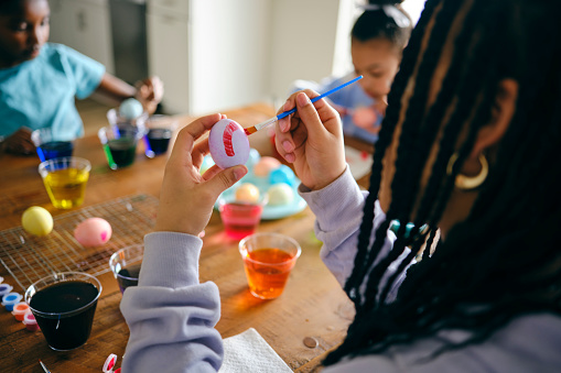 Young girls sitting at a home table, dyeing and decorating Easter eggs.