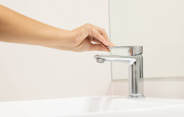 Woman push to close chrome faucet washbasin to washing hand soap for corona virus at water tap. push off water running drop off. Bathroom interior background with sink basin faucet tap. stock photo