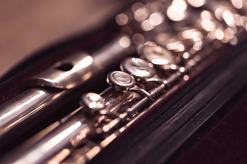 A close up portrait of a valve of a disassembled metal silver flute in a case. The musical instrument needs to be put together again in order for a flutist or musician to play a piece.