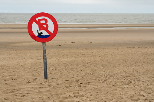 By the sea, there is a sign in the sand saying no swimming in the sea