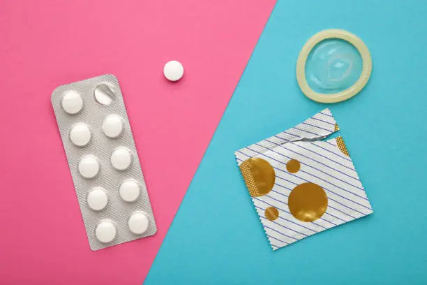 Contraceptive pills and condoms on colored background. Concept of birth control. Top view