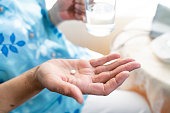 senior woman feeling sick, taking medicines in hand with a glass of water at home. Elderly and healthcare concept