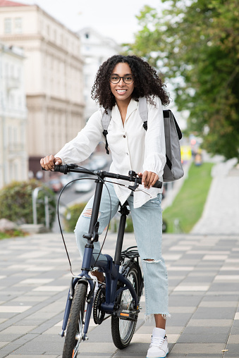 Smiling african-american woman holding a bike looking at camera outdoor. Travel, people and active lifestyle concept