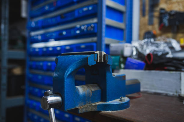 Blue bench vice over wooden table in a mechanical workshop against blue drawers.