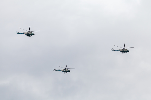 Group of three Mi-17 military Russian helicopters fliy in cloudy sky on a daytime
