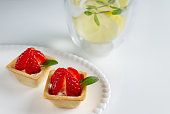 square tartlets with yogurt, strawberries and mint leaves on a white plate and a glass of water with lemon, copy space, selective focus