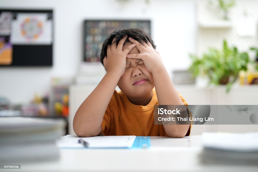 Worried young school boy studying at home Young Asian boy is tired of doing homework, sitting at the table. Child Stock Photo