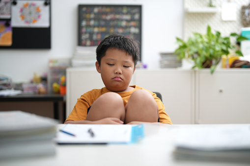 Young Asian boy is tired of doing homework, sitting at the table.