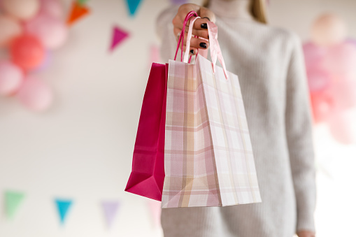 Cut out shot of a young woman standing in front of party themed background, holding paper gift bags.