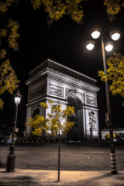 иллюминированная триумфальная арка этуаль на площади шарля де голля и елисейских полях в ночи в париже, франция - paris france night charles de gaulle arc de triomphe стоковые фото и изображения