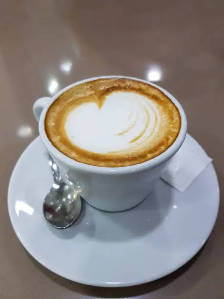 Photo of Hot coffee cup . Top view. Heart shaped milk art for the symbol of love. A mug for the morning routine.