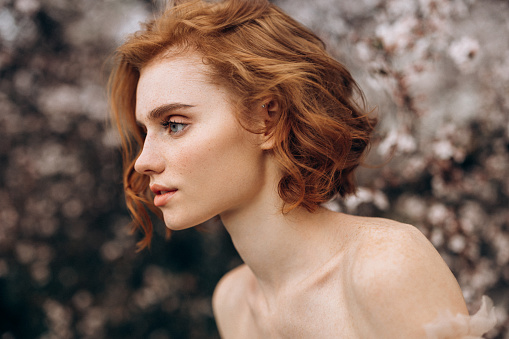 portrait of red-haired girl with long curly hair and cute freckles on beige background in the studio. Retouched photo. Skin care concept with pigmentation