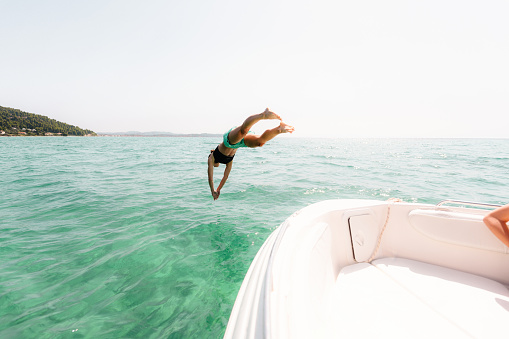Photo of a young woman jumping off the speedboat into the water and undersea diving while on summer vacation