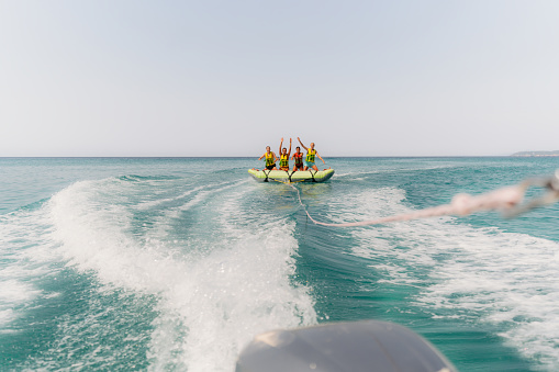 Photo of a couple of friends, who enjoy tubing session at sea on a sunny summer day. They are on an inflatable raft pulled by a speedboat.