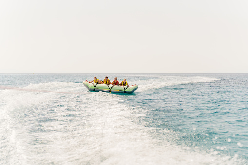 Photo of a couple of friends, who enjoy tubing session at sea on a sunny summer day. They are on an inflatable raft pulled by a speedboat.