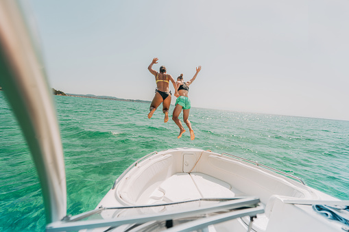 Photo of a couple of female friends having fun, jumping off the speedboat into the water and undersea diving while on summer vacation