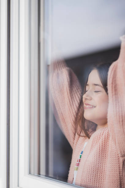 dziewczyna zamyka oczy, gdy rozciąga się przy oknie - nostalgia joy laughing wellbeing zdjęcia i obrazy z banku zdjęć