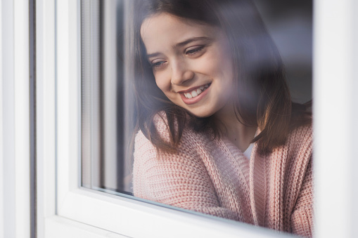 Young girl with a toothy smile looking through the window, close-up