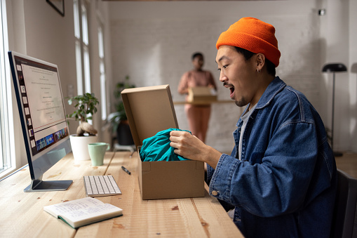 Cool looking Chinese man thrilled to open his online order at his modern apartment