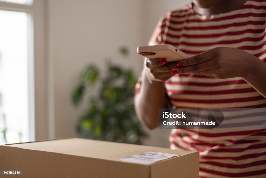 Unrecognisable black woman scanning QR code on package with her smartphone Unrecognisable African American woman scanning QR code on package with her smartphone 20-24 Years Stock Photo