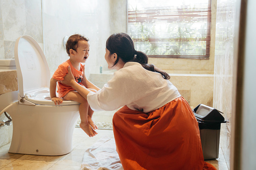 Photo of a little boy learning to use toilet amenities with a little help from his mother