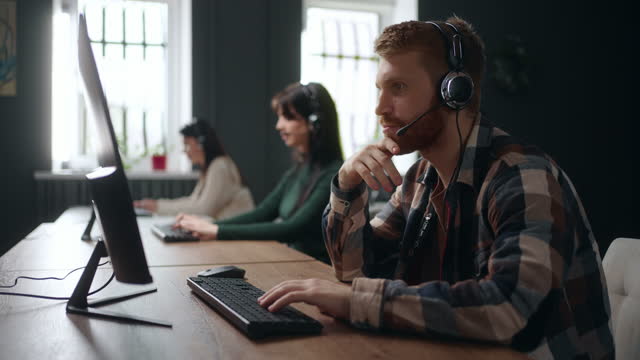 people work in call-center, young bearded man answering on phone call, consulting customers