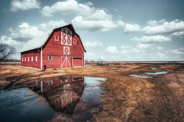 A large A framed old red barn with fresh red paint under a cloudy blue sky in a rural springtime landscape