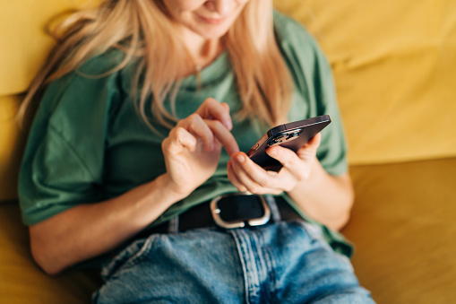 A woman sitting at home on the couch communicates online using a mobile phone.
