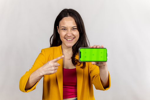 Studio shot of a young woman showing a smart phone with a green screen.
