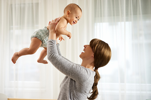 Happy young mom lifting her adorable little newborn baby boy in the air