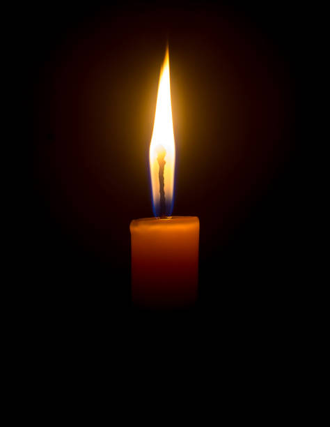istock A single burning candle flame or light glowing on an orange candle on black or dark background on table in church for Christmas, funeral or memorial service with copy space 1471206354