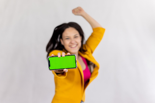 Studio shot of a young woman showing a smart phone with a green screen with raised fist.