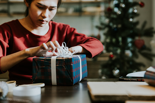 Young asian woman with hand disability checking her Christmas gift box that she wrapping by herself before giving to her friend.