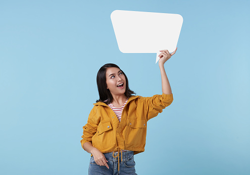 Smiling young Asian woman showing empty speech bubble in blue studio background. for advertising signs.