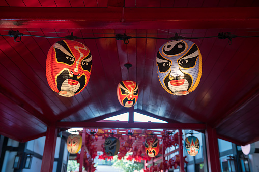 Japanese smiling Kabuki Noh mask paper lantern with light bulb hanging on red wooden ceiling.