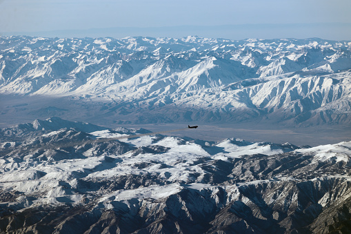 An airliner looks tiny compared to the massive landscape of California. This photo was taken above Owens Valley California with the Sierra Nevada in the distance and The White Mountain directly below.
