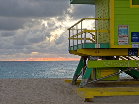Miami Beach, Florida - USA, February 2, 2023. Closeup of lifeguard hut in the pre dawn on Miami's South Beach. The lifeguard beach huts on South Beach Miami have unique paint schemes. The 6th street shack with the sun rising in background.