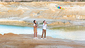 A boy and a girl launch a bright kite standing on the edge of a mountain near a pond