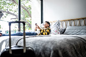 Young man using mobile phone while lying down on bed at hotel room