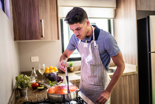 young man preparing tomato sauce in the kitchen at home - hot drink fotos imagens e fotografias de stock