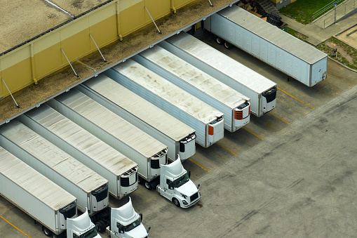 High angle view of big commercial shipping center with many freight trucks unloading and uploading goods for further distribution. Global economy concept.