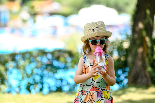 Child drinking clean tap water from transparent plastic bottle. Child girl in sunglasses with hat and colorful dress. happy 3-4 years old girl drinking water from plastic bottle. summer vacation joy. Happy child on summer vacation.