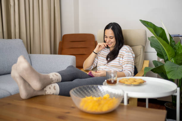 istock young lady sits on couch and laughs at something on book by extending her legs 1471247576