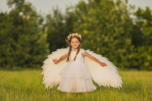 Emotional little girl in fairy costume with pink wings and magic wand on white background