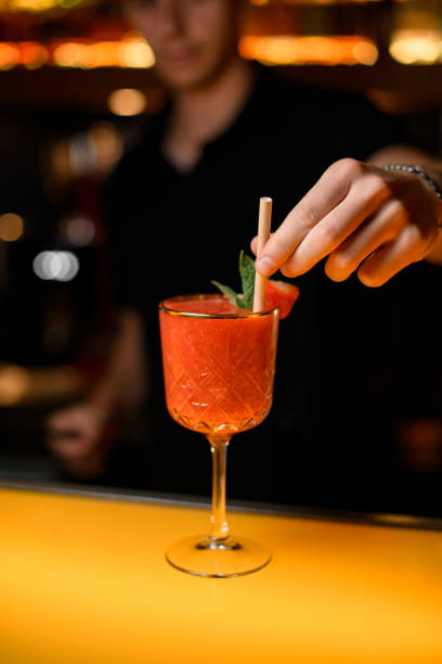 istock Hand of bartender inserts straw for drinking into crystal goblet with signature cocktail 1471254358