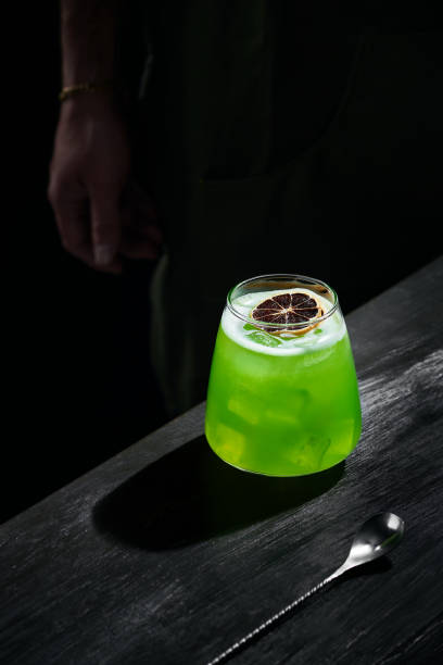 cóctel verde especial de mixología, ron de limón, adornado con frutos secos, en la mesa de bar negro, barman en el fondo - restaurante sketch fotografías e imágenes de stock