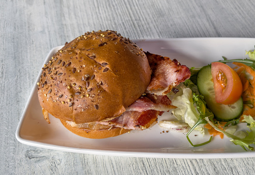 A bacon sandwich served with some salad items