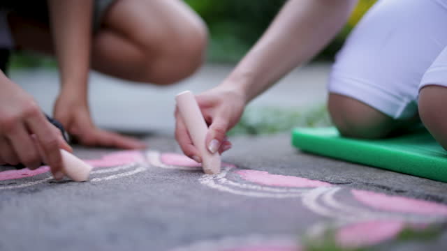 Brother and sister drawing with chalk on sidewalk in residential area