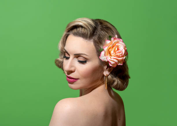 Pin up woman portrait with retro hairstyle and make up, against a green background Portrait of a beautiful young woman with a retro hairstyle and make-up, looking over her shoulder. Beautiful pin-up woman with a hair flower accessory and perfectly soft skin 40s pin up girls stock pictures, royalty-free photos & images