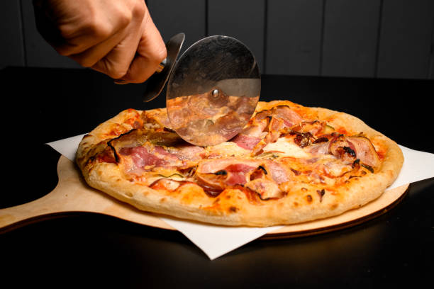 istock hand cuts with a pizza cutter round pizza with bacon on wooden chopping board 1471269667